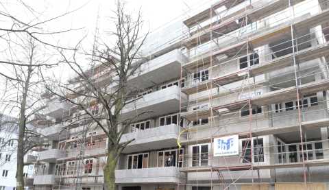 Mehrstöckiges Gebäude im Rohbau mit Gerüst und zwei kahlen Bäumen davor.