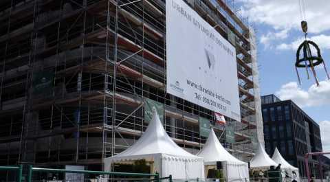 Baustelle mit Gerüst, weißen Zelten und Richtkranz vor blauem Himmel.