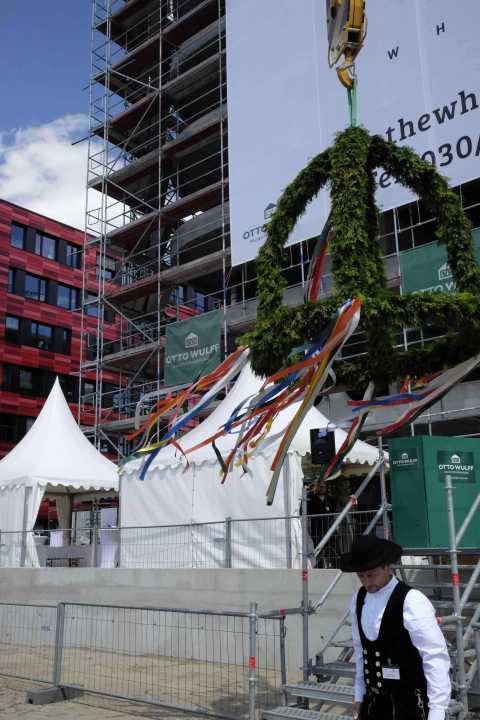Richtfest-Kranz mit bunten Bändern vor Baustelle und weißen Festzelten.