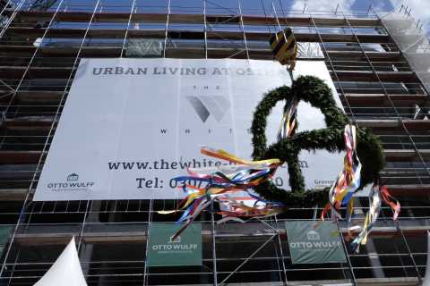 Kranz mit bunten Bändern hängt an Baugerüst vor Banner mit Werbung für Neubau.