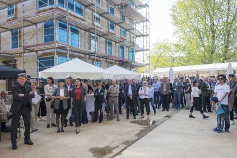 Menschen stehen vor einem Rohbau und weißen Pavillons bei einer Veranstaltung.
