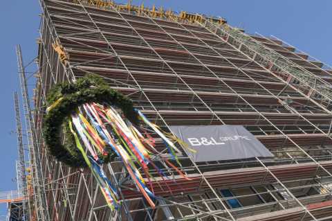 Richtkranz mit bunten Bändern an eingerüstetem Neubau unter blauem Himmel.