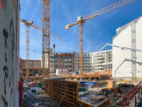Großbaustelle mit mehreren Kränen, Wohnhäusern und Baugerät bei Sonnenschein.