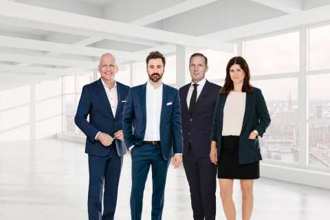 Vier Personen in Businesskleidung stehen in einem modernen, hellen Büro.