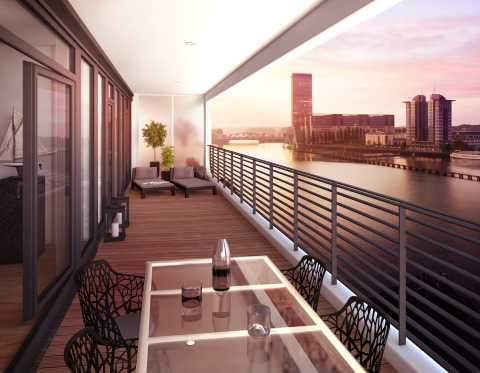 Moderne Terrasse mit Glasgeländer, Lounge-Möbeln und Blick auf den Fluss bei Sonnenuntergang.