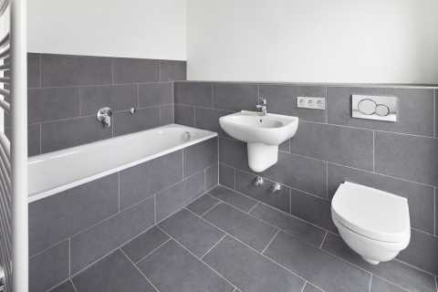 Modernes, graues Bad mit Badewanne, Waschbecken und wandhängender Toilette.