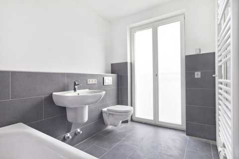 Modernes, helles Bad mit grauen Fliesen, Waschbecken, WC und Fenster.