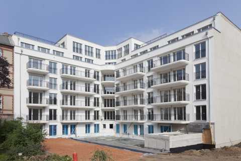 Neubau eines modernen, weißen Mehrfamilienhauses mit Balkonen und Baustelle.