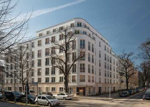 Modernes, weißes Eckwohnhaus mit großen Fenstern, Autos und kahlen Bäumen.