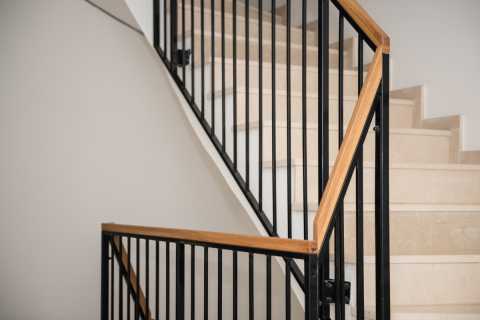 Helle Steintreppe mit schwarzem Metallgeländer und Holz-Handlauf in Innenraum.