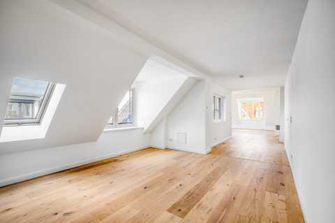 Helles Dachgeschoss mit Holzfußboden, weißen Wänden und großen Fenstern.