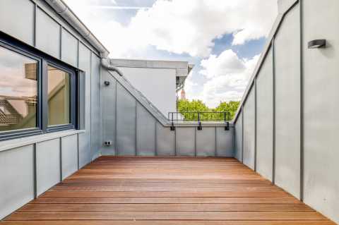 Moderne Dachterrasse mit Holz­boden und Blick auf Bäume und Himmel.