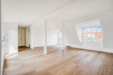 Helles, leeres Dachgeschoss mit Holzfußboden, weißen Wänden und Fenstern.