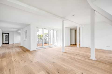 Helles, leeres Wohnzimmer mit Holzboden und großen Fenstern zur Terrasse.