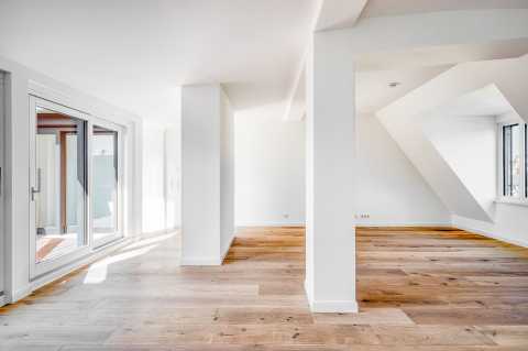 Helles, leeres Zimmer mit Parkettboden, weißen Wänden und großen Fenstern.