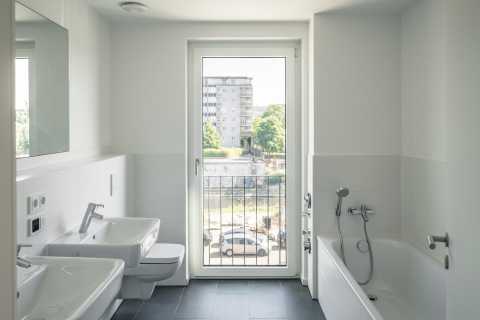 Helles Bad mit zwei Waschbecken, Badewanne und großer Tür zum Balkon.