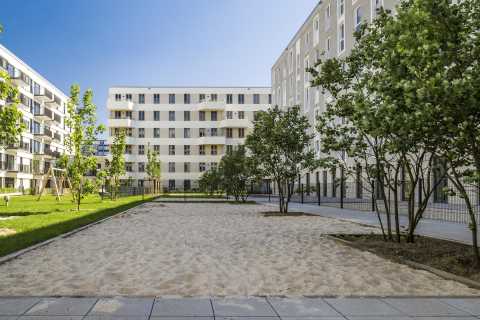 Moderner Innenhof mit Sandfläche, Bäumen und Rasen zwischen Wohngebäuden.