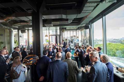 Menschen bei einer Veranstaltung in moderner Location mit Stadtblick und Fenstern.