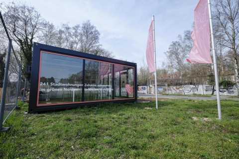 Moderner Containerbau mit Glasfront und zwei pinken Fahnen im Grünen.