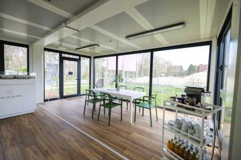 Heller Raum mit Tisch, vier grünen Stühlen und Servicewagen mit Getränken.