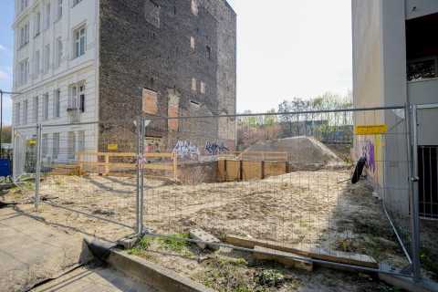 Eingezäunte Baustelle zwischen zwei Häusern mit Sandhaufen und Graffiti.