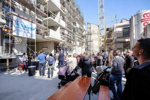 Menschenmenge bei sonnigem Wetter vor Baustelle mit Gerüsten und Kinderwagen.