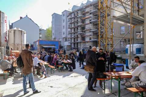 Menschen sitzen an Tischen auf einer Baustelle und genießen gemeinsam Essen.