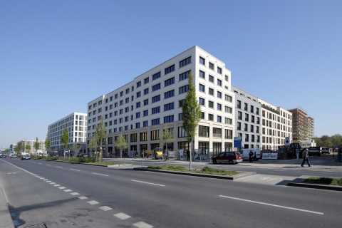 Neubau eines modernen Bürogebäudes an einer breiten Straße mit Gehweg und Bäumen.