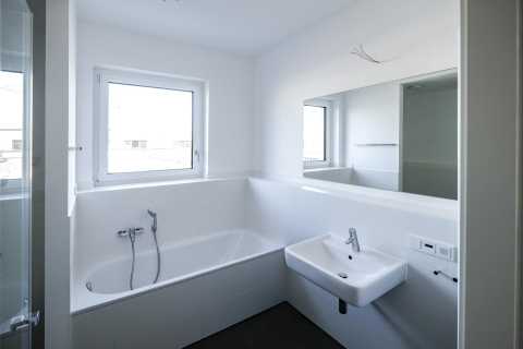 Modernes, weißes Badezimmer mit Badewanne, Fenster, Waschbecken und Spiegel.