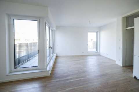 Heller leerer Raum mit großen Fenstern und Holzfußboden.