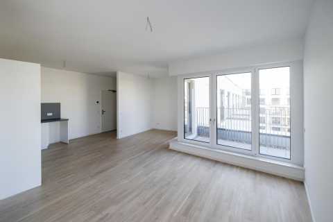 Helles, leeres Zimmer mit Parkettboden und bodentiefen Fenstern zum Balkon.