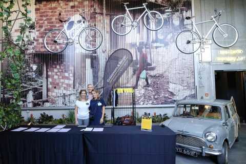 Drei Frauen am Empfang, Fahrräder hängen über einem alten Auto an der Wand.