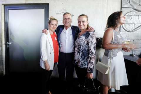 Drei Menschen posieren lächelnd, daneben steht eine Frau mit Weinglas.