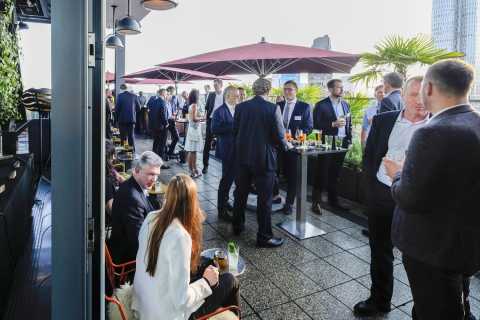 Menschen im Business-Outfit unterhalten sich bei einem Empfang auf einer Terrasse.