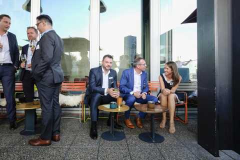 Mehrere Menschen im Anzug unterhalten sich auf einer Terrasse bei Tageslicht.
