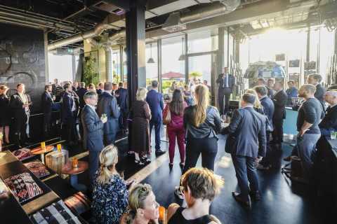 Menschen in Businesskleidung auf einer Veranstaltung mit Redner in modernem Raum.