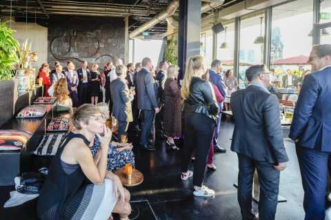 Viele Menschen in Businesskleidung bei einer Veranstaltung in modernem Innenraum.