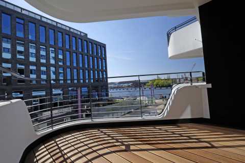 Große Terrasse mit Holzboden, Blick auf modernes Gebäude und Fluss im Hintergrund.