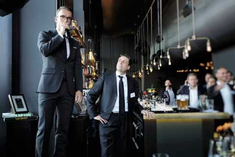 Ein Mann im Anzug spricht in einer Bar ins Mikrofon, andere hören zu.