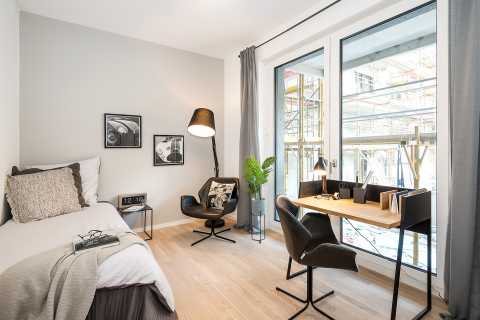 Modernes, helles Zimmer mit Bett, Schreibtisch, Sessel und großer Fensterfront.