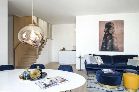 Modernes Wohnzimmer mit blauem Sofa, runder Lampe und großem Porträt an der Wand.