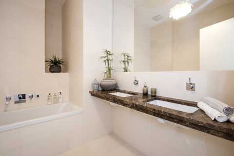 Modernes Bad mit Doppelwaschbecken, Badewanne und Pflanzen auf Ablagen.