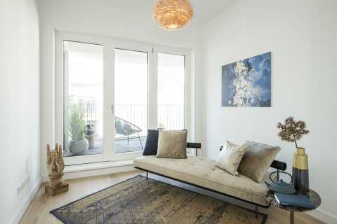 Modernes, helles Zimmer mit Liege, Kunstwerk, Teppich und Balkon im Hintergrund.