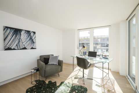 Helles Arbeitszimmer mit Glas-Schreibtisch, Sessel und abstraktem Bild an der Wand.