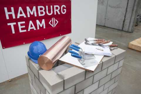 Mauer, Bauhelm, Kupferrolle, Bauwerkzeuge und Unterlagen vor Hamburg-Team-Banner