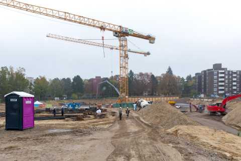Baustelle mit zwei Kränen, Bagger, Bauarbeitern und einem mobilen WC.