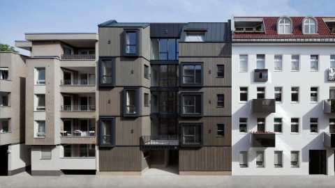 Modernes Wohnhaus mit dunkler Fassade zwischen zwei klassischen Gebäuden.