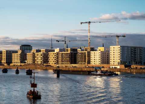 Wohnhäuser am Wasser mit Baukränen und Schiff bei Sonnenuntergang.
